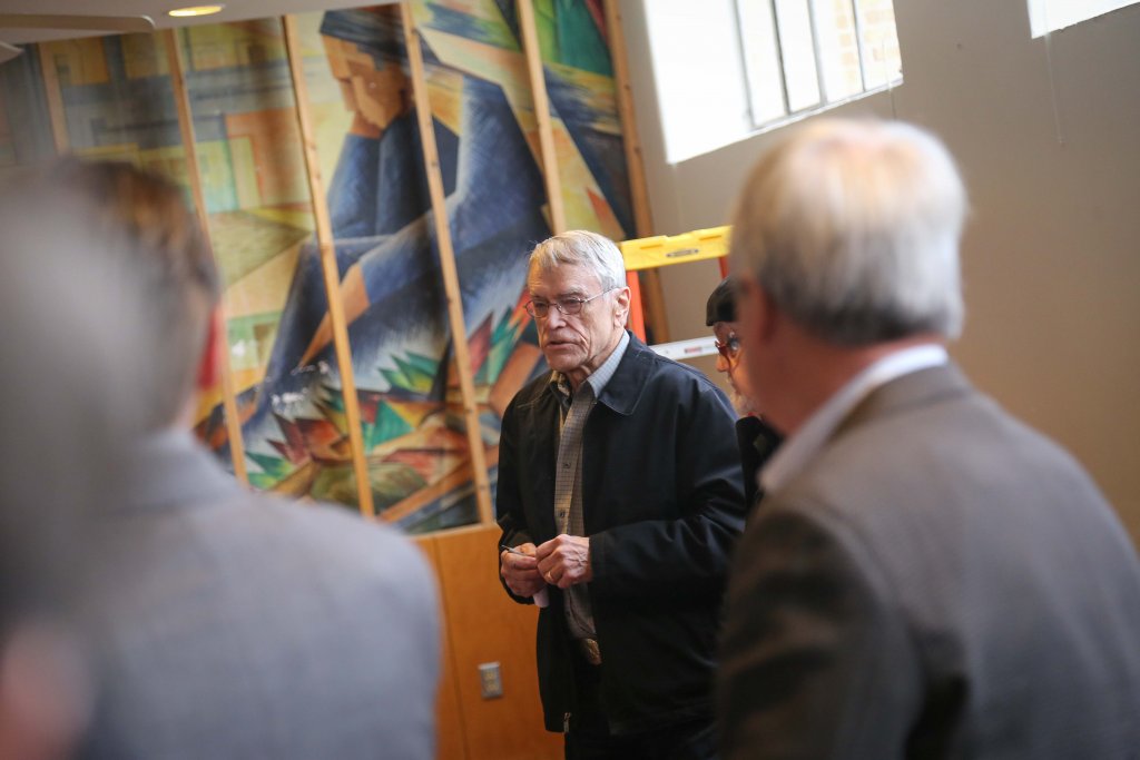 Man speaking to a group in front of a painting